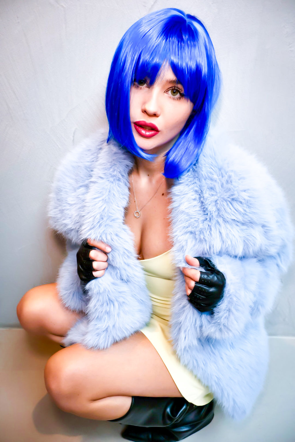Person with blue wig and fur coat posing on a light background