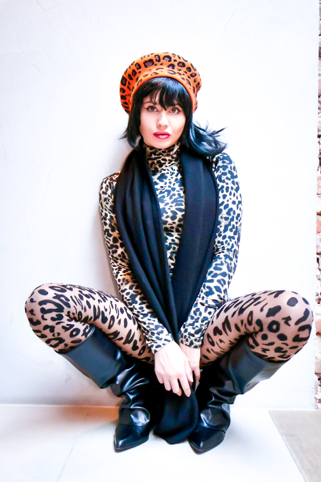 Person wearing a leopard print outfit with a blue scarf and black boots on a white background
