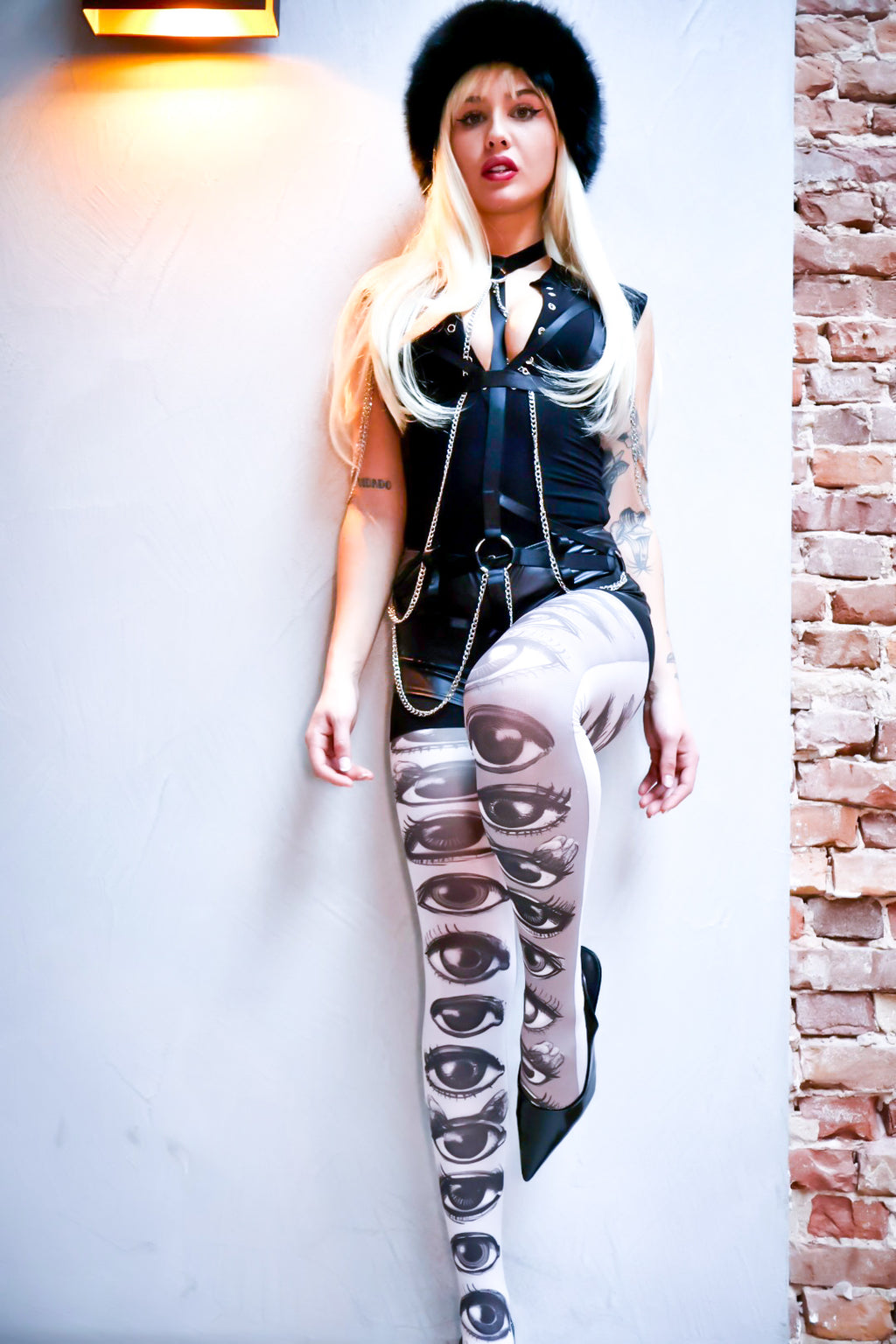 Person wearing a black leather outfit with a unique design on a white wall.